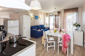 Una cocina moderna con estufa, cafetera y refrigerador. Hay un comedor con mesa, sillas y un sofá azul.