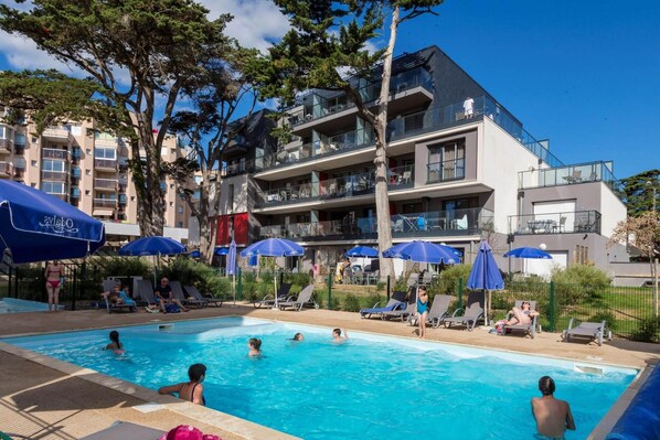 Ein Pool mit Liegestühlen und Sonnenschirmen, umgeben von mehrstöckigen Gebäuden mit Balkonen.
