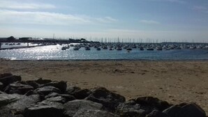 Ein Strand mit steiniger Uferböschung und einer Marina im Hintergrund.