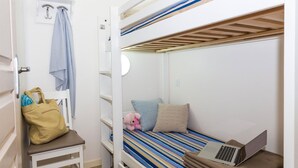 Ein Schlafzimmer mit Etagenbetten, ein Laptop auf dem untere Bett, ein Teddybär und eine Tasche auf einem Stuhl.