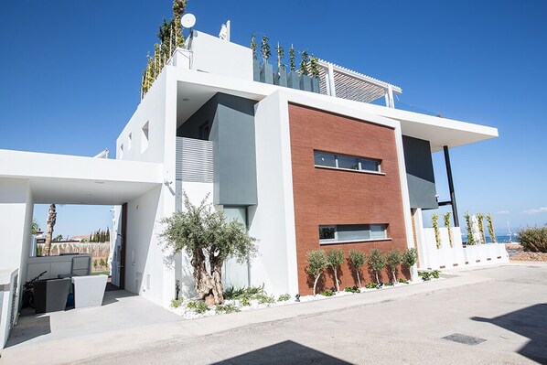 A modern two-story building with a flat roof, large windows, and a balcony with plants. - Villa Chana, Luxury 4BDR Villa with Private Pool, Hot Tub and Sea Views (Protaras)