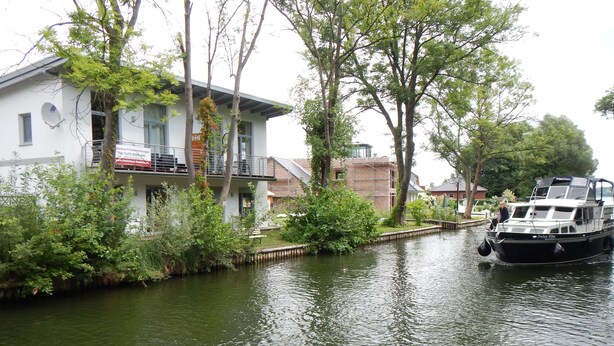 Un río con un bote amarrado a la derecha, rodeado de vegetación y un edificio con balcones.