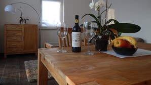 Una mesa de comedor con una botella de vino, dos copas de vino, un frutero y una orquídea en maceta.