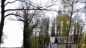 Un lago tranquilo con un muelle de madera, una casa con techo de tejas y un cartel de estacionamiento 'R'.