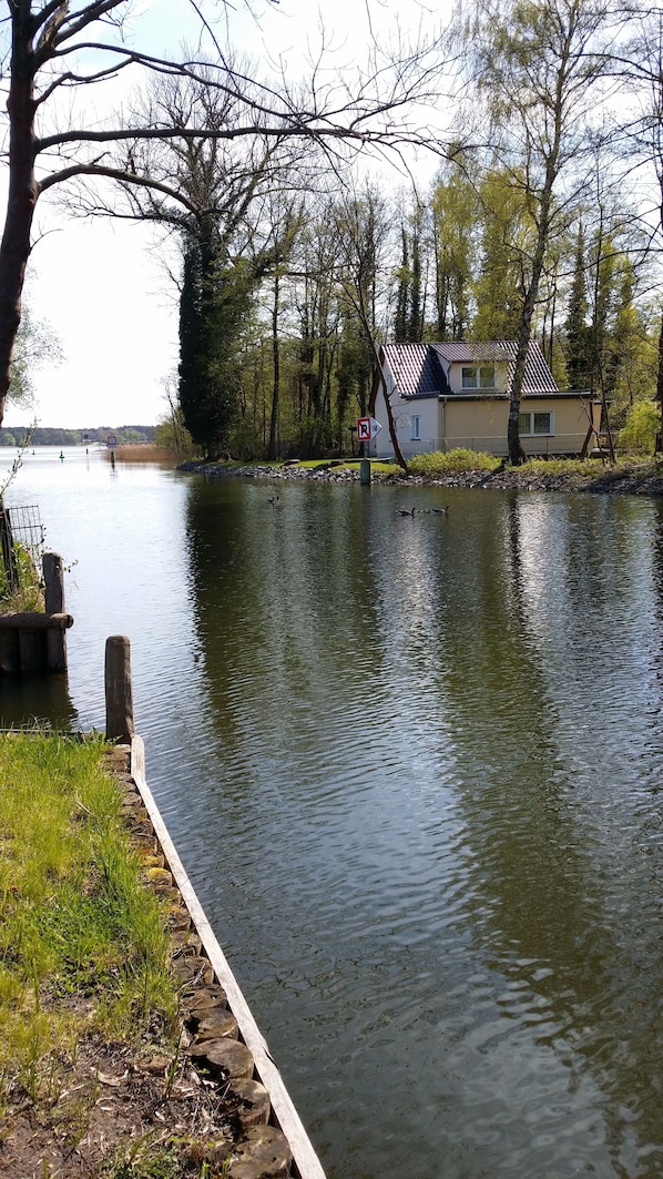 A calm lake with a wooden dock, a house with a tiled roof, and a 'R' parking sign.
