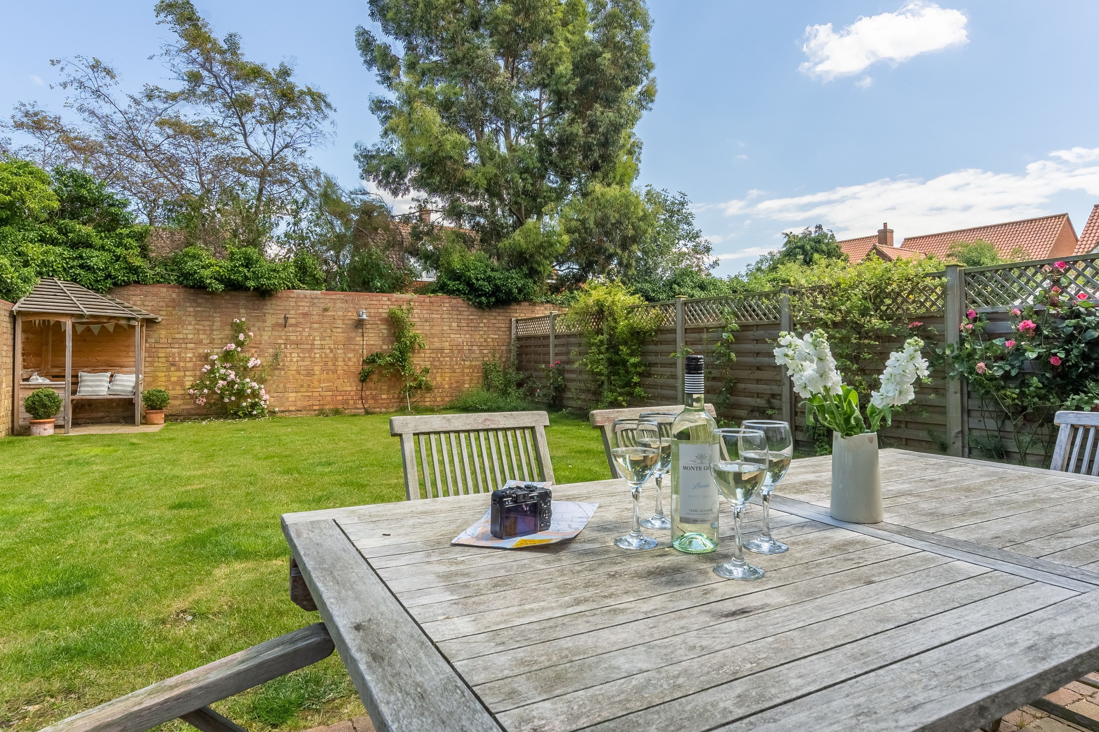 A wooden table set outdoors with a bottle of wine, glasses, and a cake.