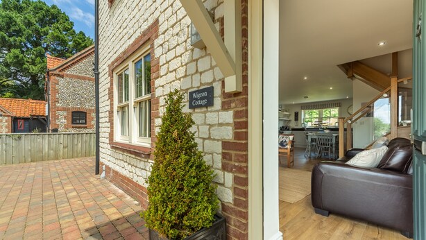 A cottage with a brick exterior, a wooden deck, a potted plant, and a leather sofa.