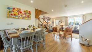 A dining area with a wooden table and chairs, a staircase, and a living room with a sofa and a dog statue.