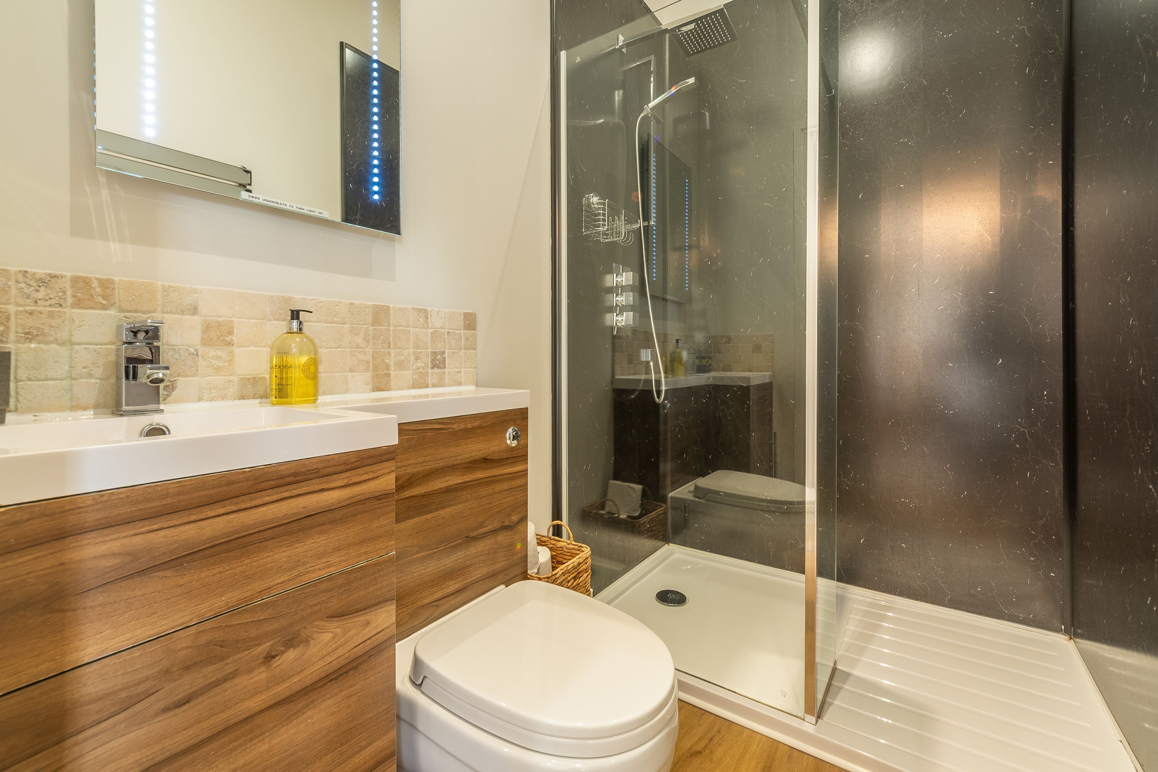 A modern bathroom with a glass shower enclosure, a wooden vanity, and a white toilet.