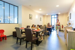 A dining area with tables and chairs, a kitchen area with a coffee machine, and a window with a view.