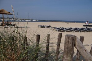 A beach with sun loungers, a wooden fence, and a thatched umbrella.