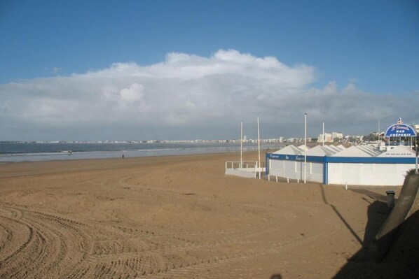 A beach with a row of beach huts and a clear sky.