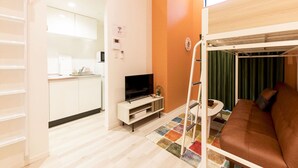 A room with a bunk bed, a TV, a small kitchenette, and a colorful rug. - Trip Pod Yoshizuka B (Fukuoka)