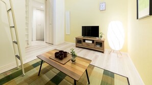 A living room with a wooden coffee table, a TV on a wooden stand, a ladder, and a door leading to another room. - Trip Pod Yoshizuka B (Fukuoka)