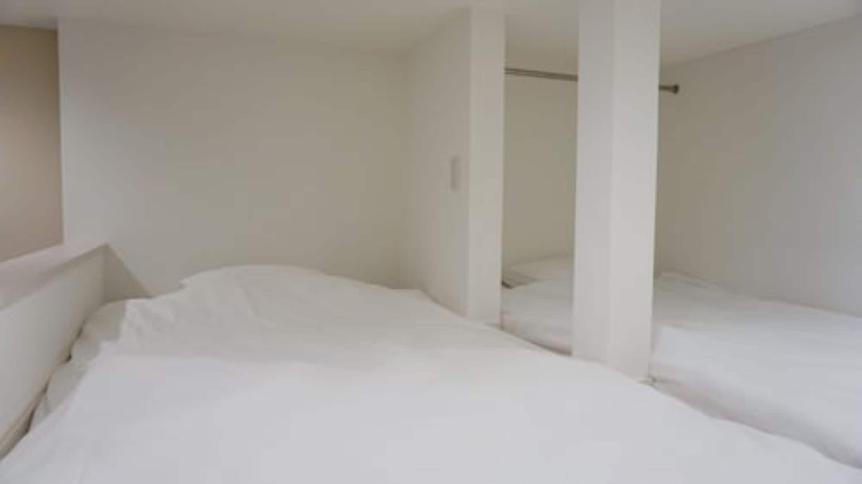 Una habitación con dos camas, paredes blancas y una puerta visible que da a otra habitación.