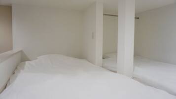 Una habitación con dos camas, paredes blancas y una puerta visible que da a otra habitación.