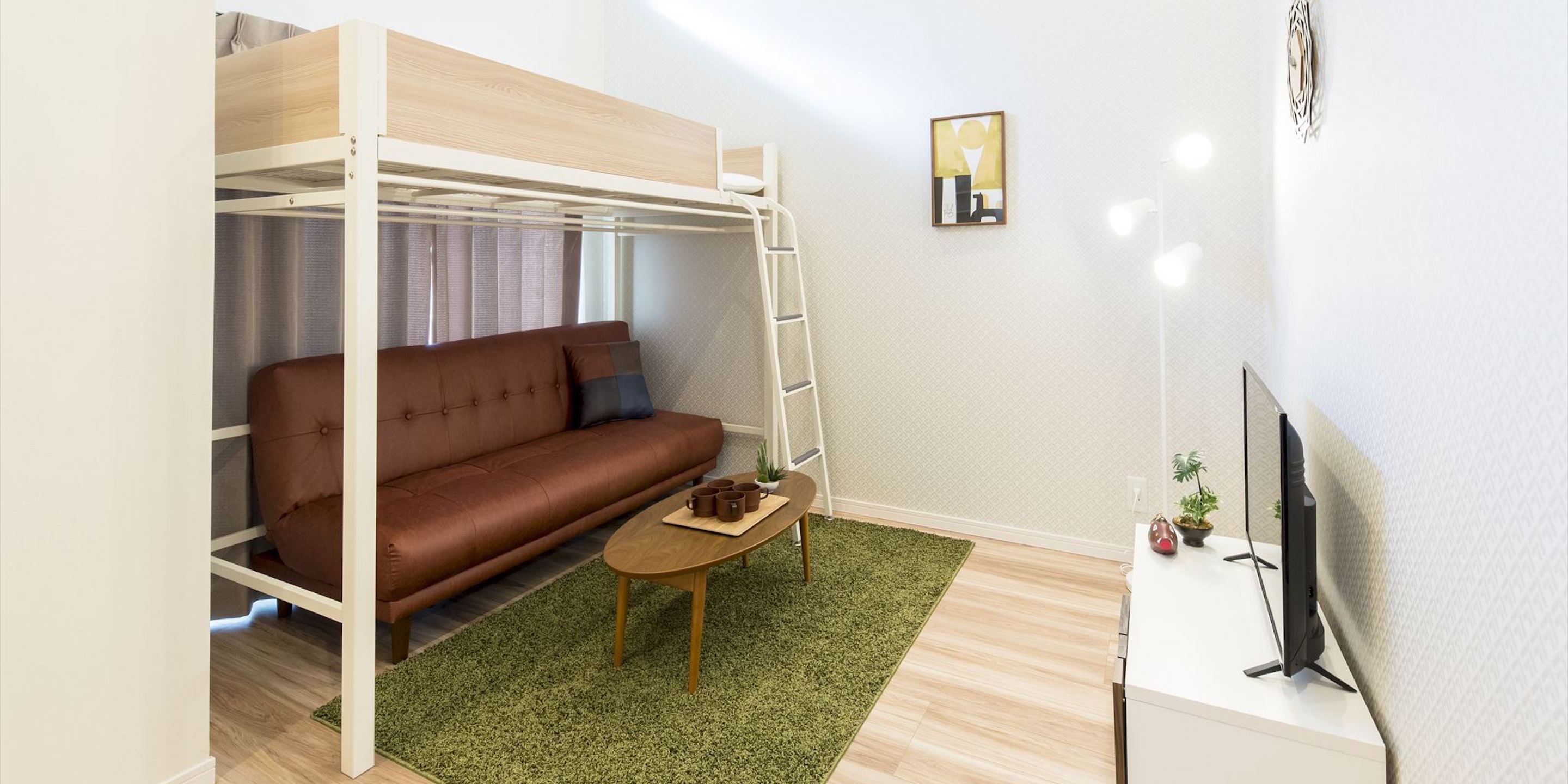 A compact room with a bunk bed, a sofa, a small table, a TV, and a few plants.
