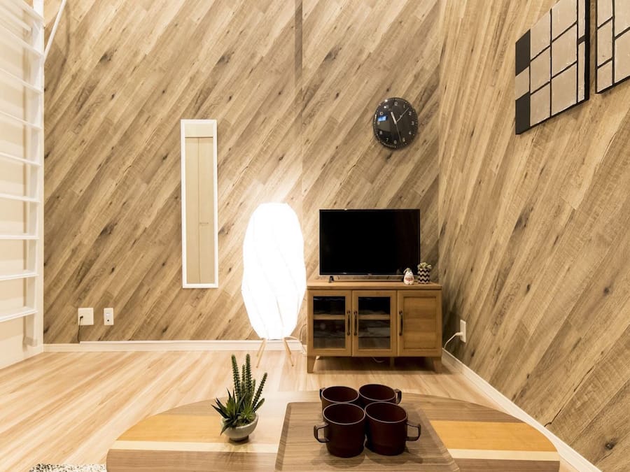 A modern living room with a wooden wall, a flat-screen TV, a cabinet, a plant, and a coffee table.
