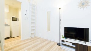 Un salon moderne avec un téléviseur à écran plat, un meuble de rangement blanc, une lampe sur pied et une armoire blanche.