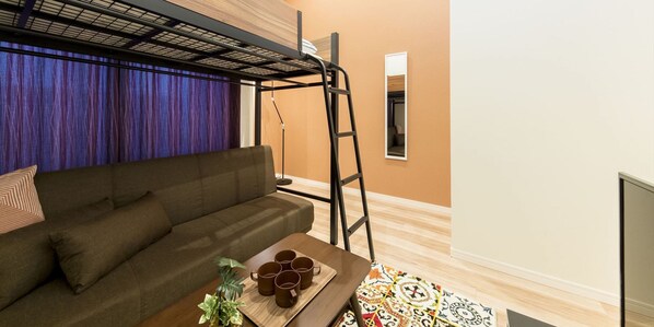 Une pièce avec un lit superposé, un canapé, une petite table avec des tasses et un miroir au mur.