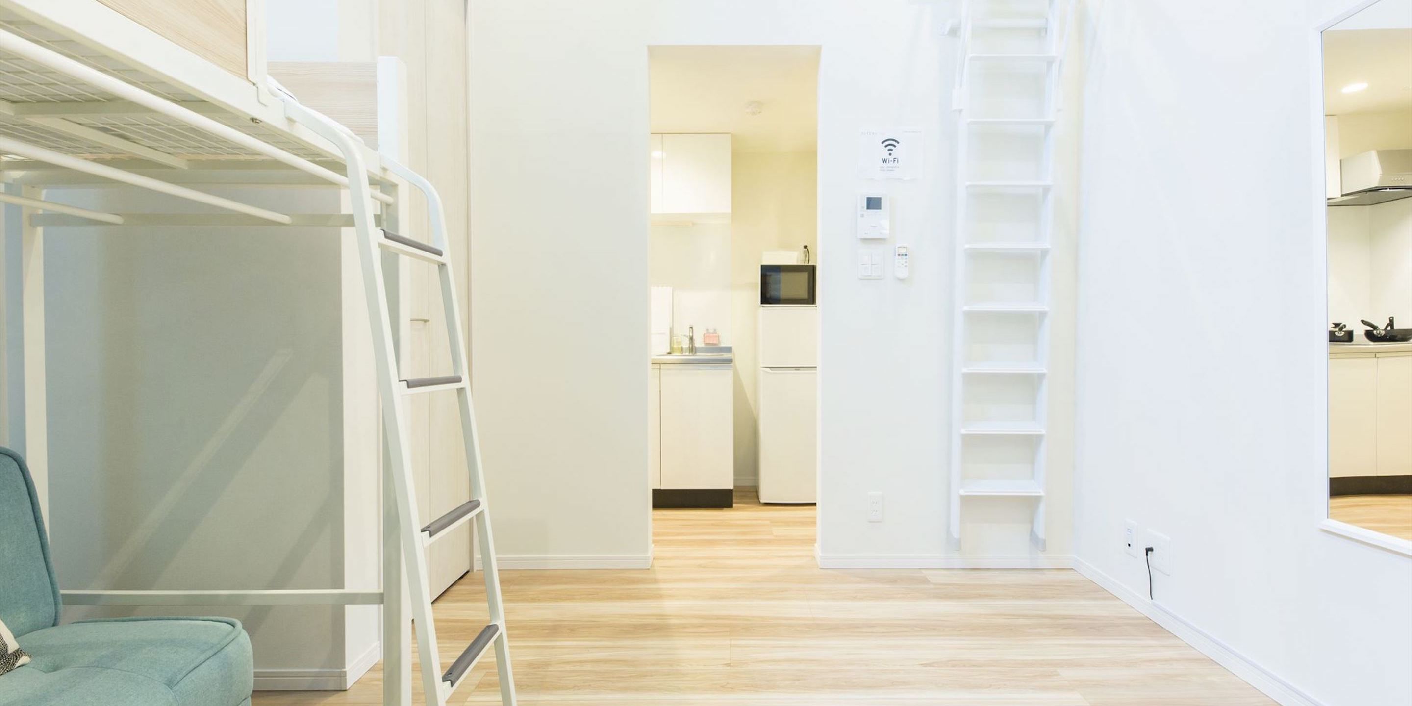 A modern hotel room with a bunk bed, a kitchenette, and a white interior.