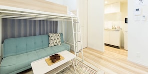 Une pièce compacte comprenant un lit superposé, un canapé, une petite table avec des tasses, un coin cuisine et un panneau indiquant la présence d’une connexion Wi-Fi.