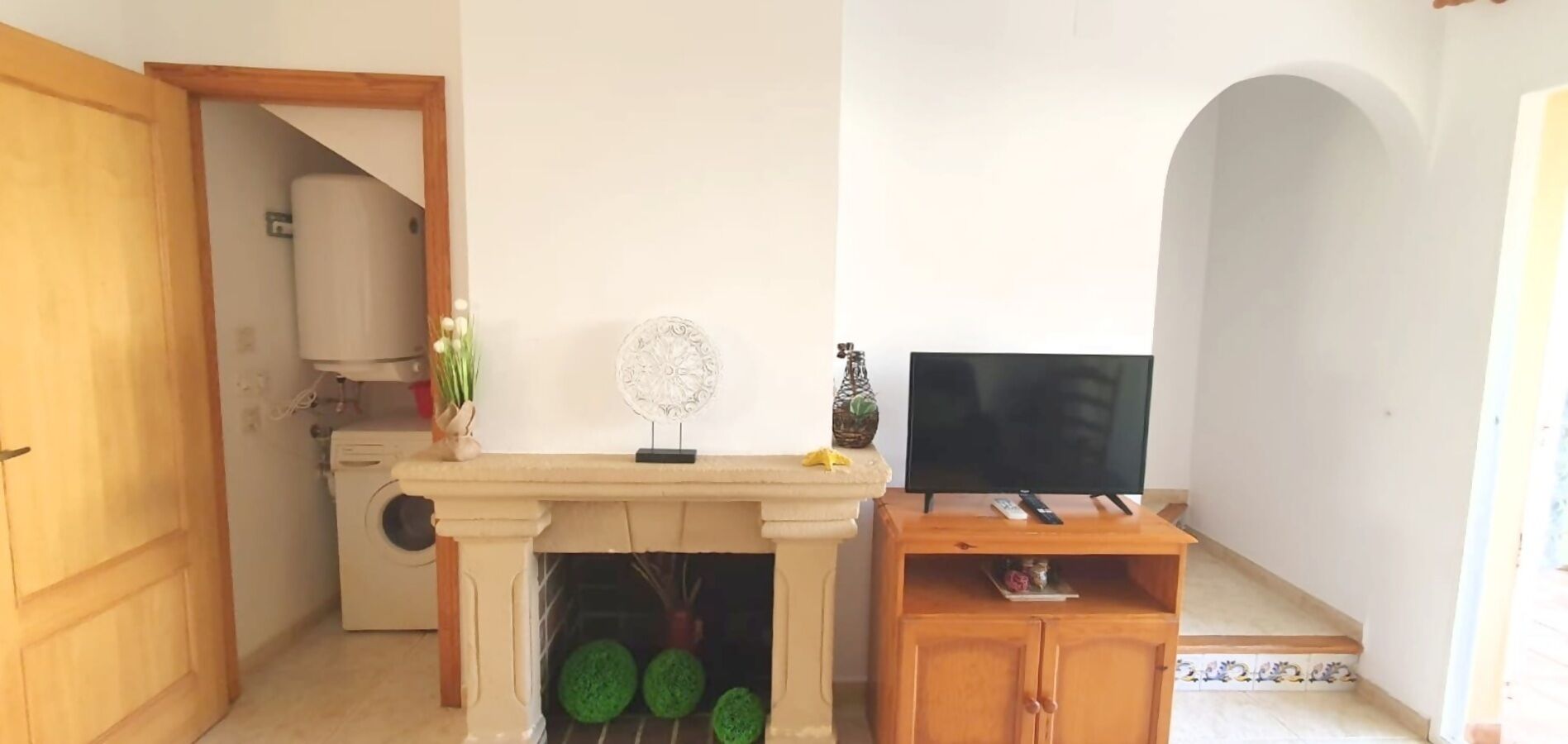 A living room with a fireplace, a television on a wooden stand, and a door leading to another room.