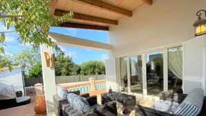 Un patio techado con mobiliario de mimbre, piscina y vistas del paisaje circundante.