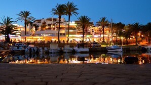 Un puerto deportivo con barcos amarrados, un paseo marítimo y edificios con letreros iluminados.