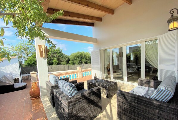 A covered patio area with wicker furniture, a pool, and a view of the surrounding landscape.