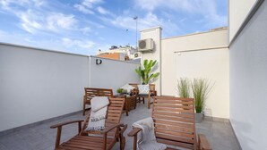 Eine Dachterrasse mit Holzliegen, einem kleinen Tisch und einem Topfpflanzen.