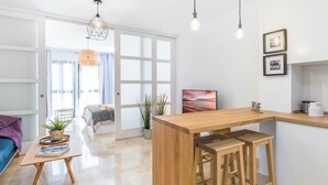 Eine moderne Küche mit einer Holzanbar und Barhocker, ein Essbereich mit Tisch und Stühlen sowie ein großes Fenster mit Blick ins Freie.