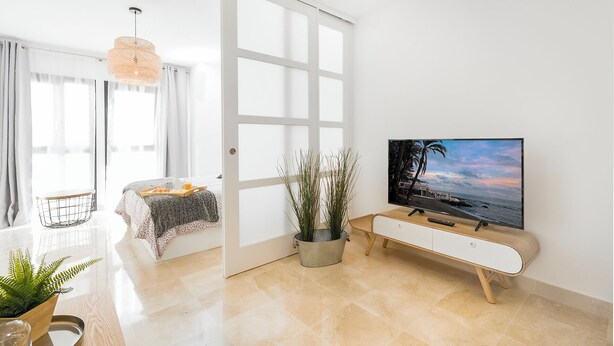 Ein modernes Wohnzimmer mit Fernseher, einer Essecke mit Tisch und Stühlen und einer Schiebetür, die in einen anderen Raum führt.