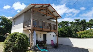 Ein zweistöckiges Haus mit Holzbalkon, überdachter Terrasse und kleinem Garten.