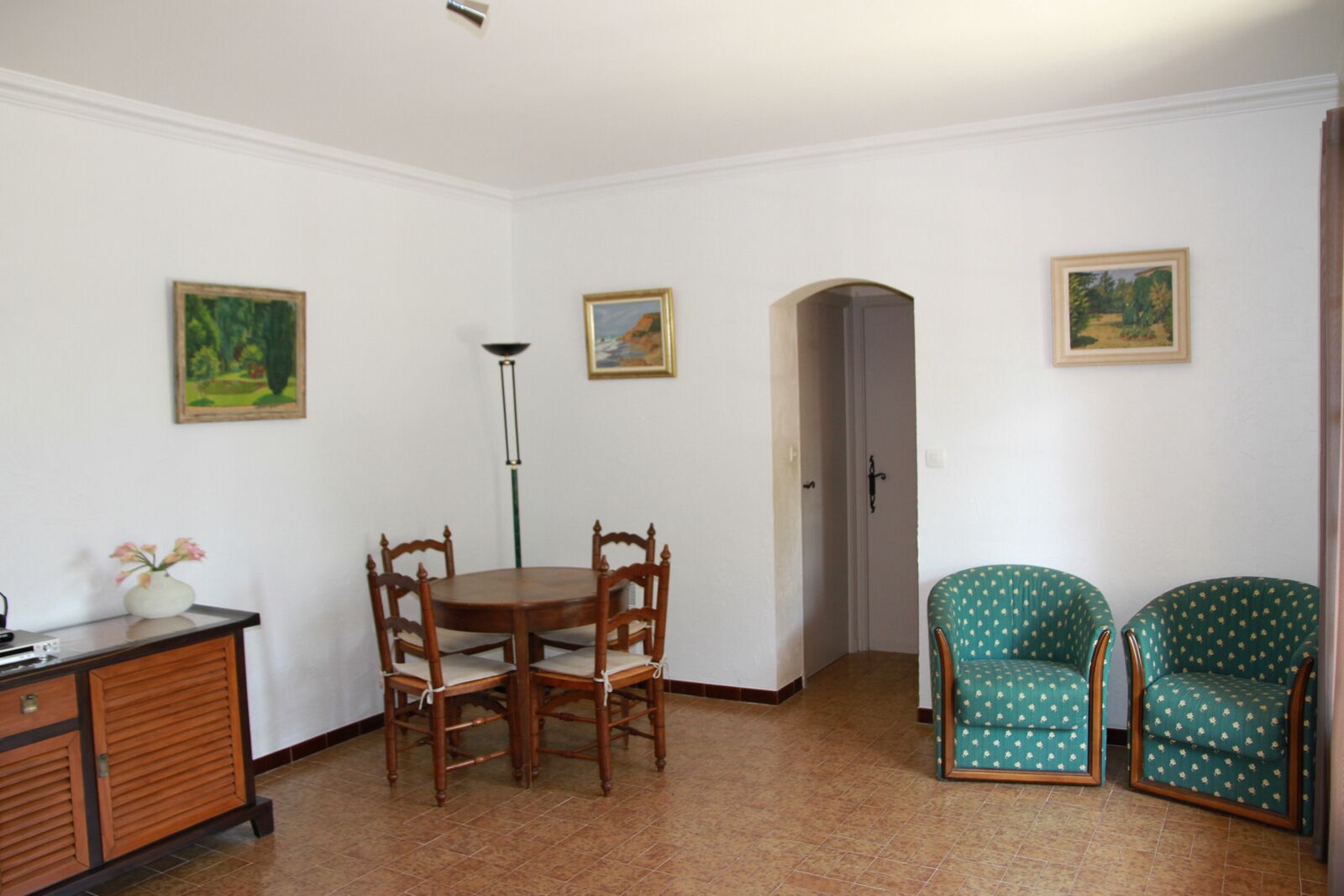A dining area with a wooden table and chairs, a floor lamp, and two green patterned armchairs.