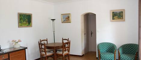 A dining area with a wooden table and chairs, a floor lamp, and two green patterned armchairs.