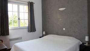 Une chambre avec un grand lit, une fenêtre avec des rideaux, une lampe fixée au mur et un radiateur.