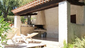 Une terrasse extérieure dotée d’un sol en pierre, d’une pergola en bois et d’un barbecue encastré.