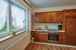 A kitchen with wooden cabinets, a built-in oven, a dishwasher, and a window with sheer curtains.