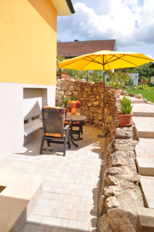 An outdoor patio with a stone wall, a yellow umbrella, and a table with chairs.
