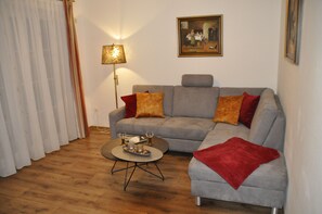 Ein Wohnzimmer mit einem grauen Sofa, einer roten Decke, einer Stehlampe und einem Bild an der Wand.