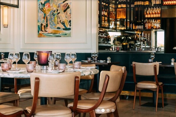A restaurant interior with a bar area, dining tables, chairs, and a large abstract painting on the wall.