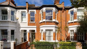 A Victorian-style terraced house with bay windows, a front garden, and a black metal fence.