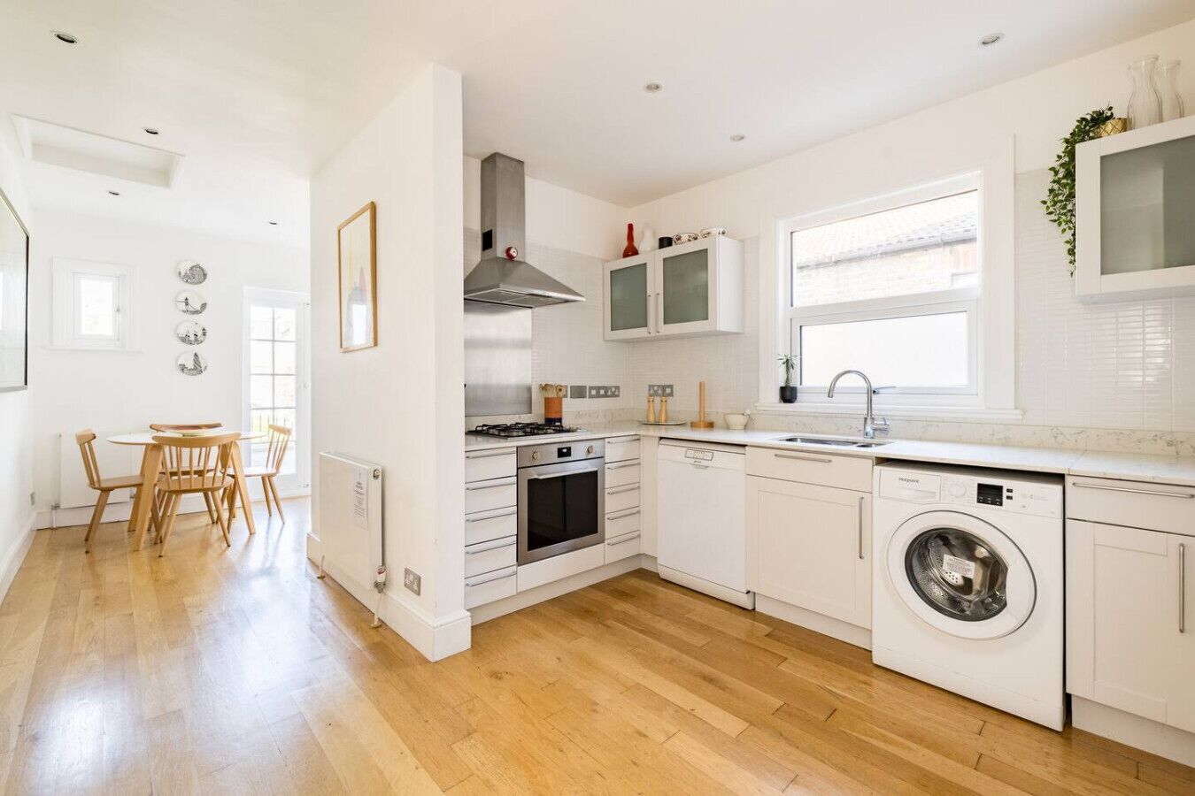 A modern kitchen with white cabinetry, a built-in oven, a stove, a dishwasher, and a washing machine.