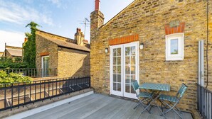 A brick building with a wooden deck, a table with chairs, and a window with a view.