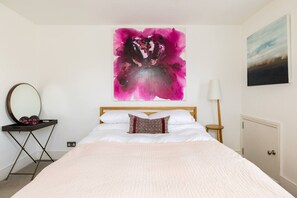 A bedroom with a bed, a mirror, a lamp, and artwork on the walls.