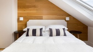A bedroom with a sloped ceiling, a wooden wall, a bed with white bedding, two bedside tables, and a skylight.