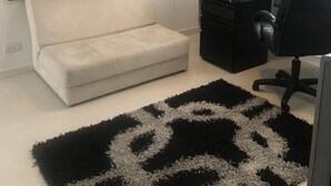 Quarto com cama, escrivaninha com cadeira, tapete preto e branco e um quadro na parede.