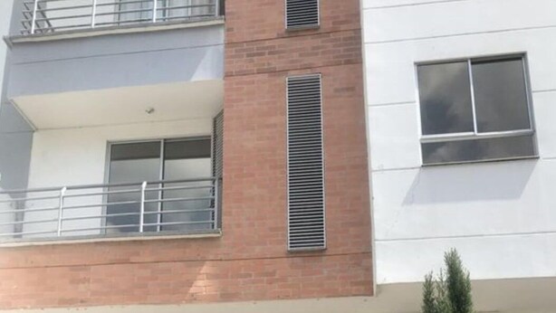 Um edifício de vários andares com design moderno, apresentando uma combinação de fachadas de tijolo e concreto, grandes janelas e uma unidade de ar condicionado visível.