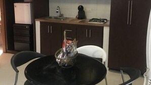 Uma cozinha compacta com armários escuros, uma pequena mesa de jantar com quatro cadeiras e uma geladeira.